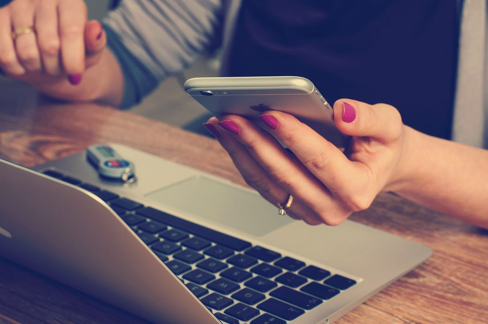 Hands holding a phone above a laptop keyboard