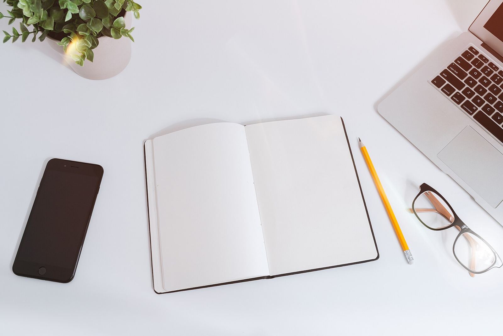 Notebook, phone and laptop on a white desk